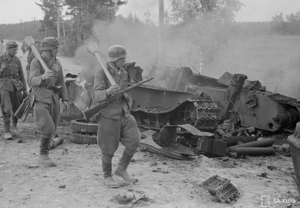 Suomalaiset sotilaat ohittavat panssarinyrkit olalla tuhotun venäläisen T 34-panssarin Ihantalassa 30.6.1944. Kuvan vaunun tuhosi saksalainen rynnäkkötykki Sturmgeschütz III. SA-kuva