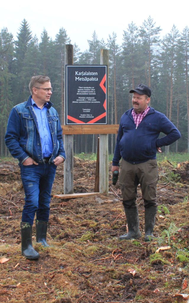 Karjalan Liiton pj Pertti Hakanen ja Mustialan yhteismetsän pj Pekka Ahokas Karjalaisen muistometsän paikalla Tammelassa. ”Tämä metsäpalsta on istutettu Karjalan Liiton 80-vuotisjuhlauoden ja siirtokarjaisten kunniaksi”, lukee juuri pystytetyssä taulussa.